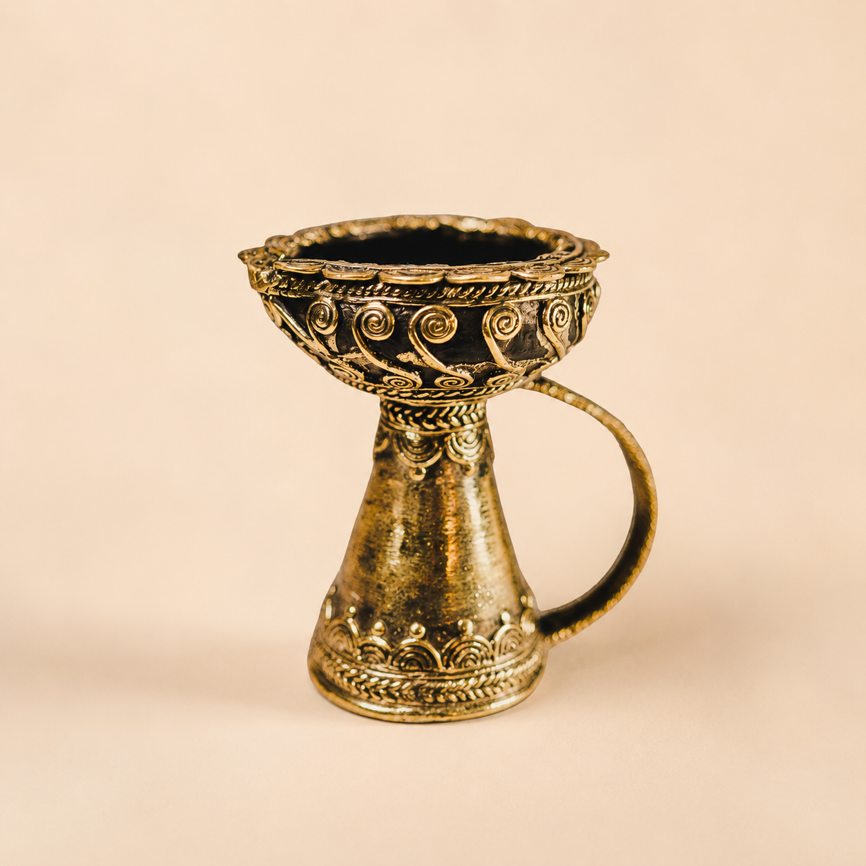 Dhokra brass diya with spiral wirework on a warm ivory studio background