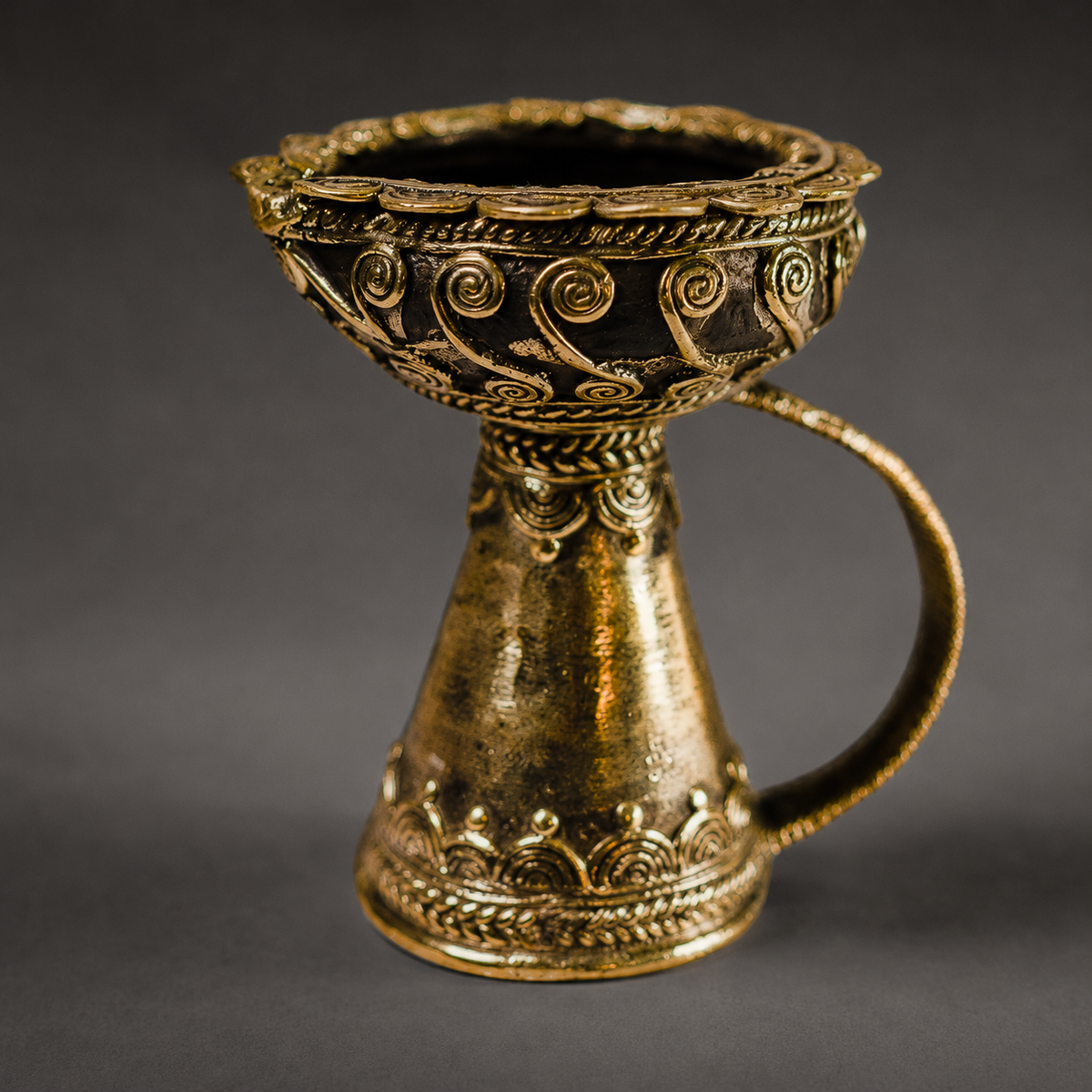 Detailed Dhokra diya showing spiral wirework, casting texture and brass patina