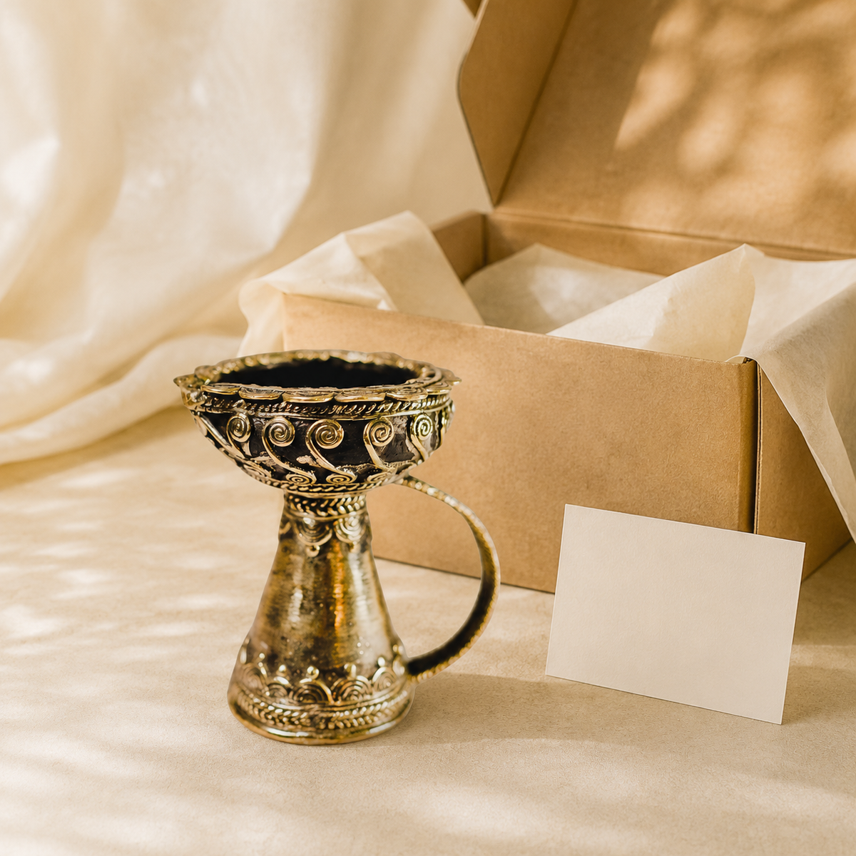 Dhokra brass diya beside an open kraft gift box and blank card for scale