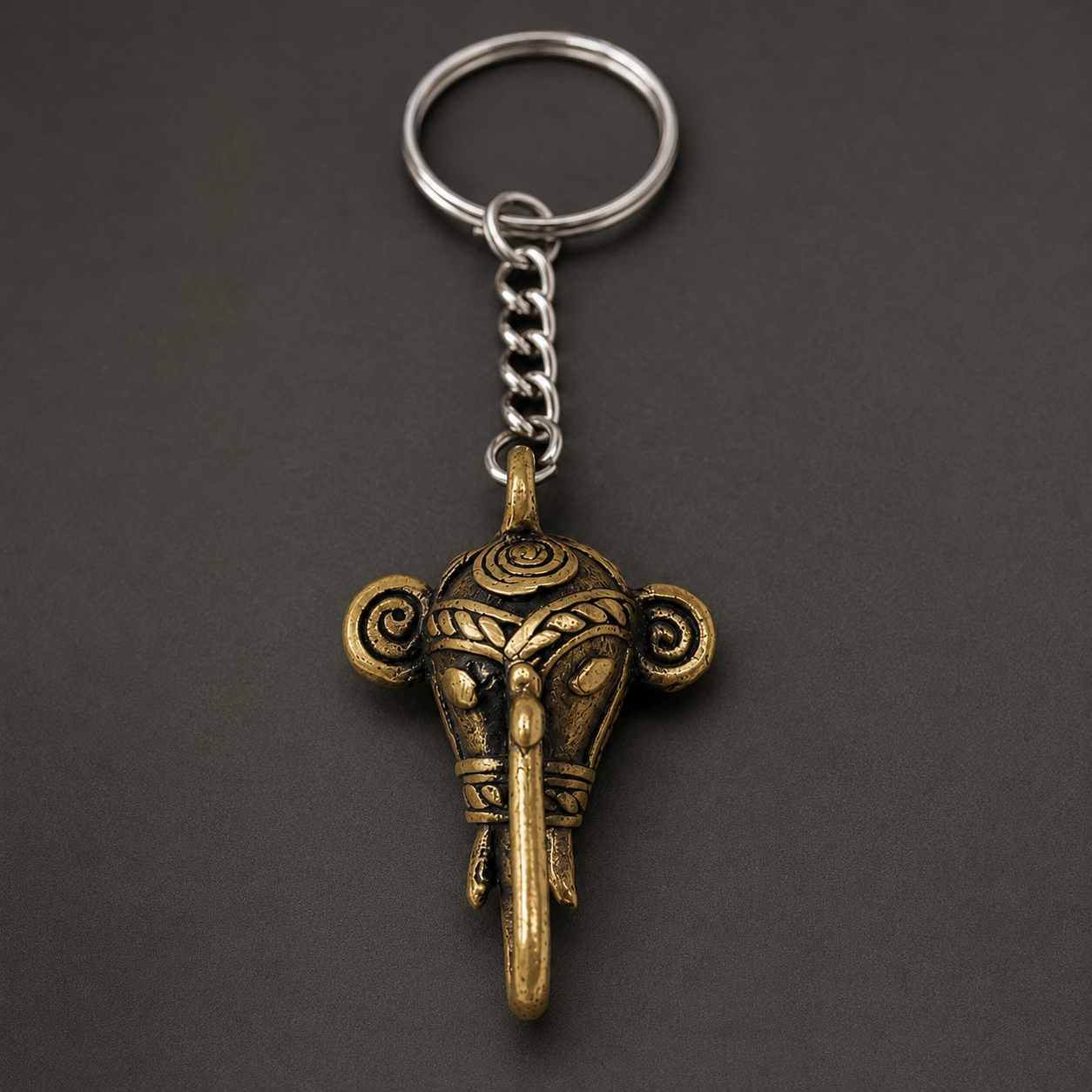 Close detail of the spiral ears, engraved bands, long trunk, and antique brass patina of a Dhokra elephant keyring