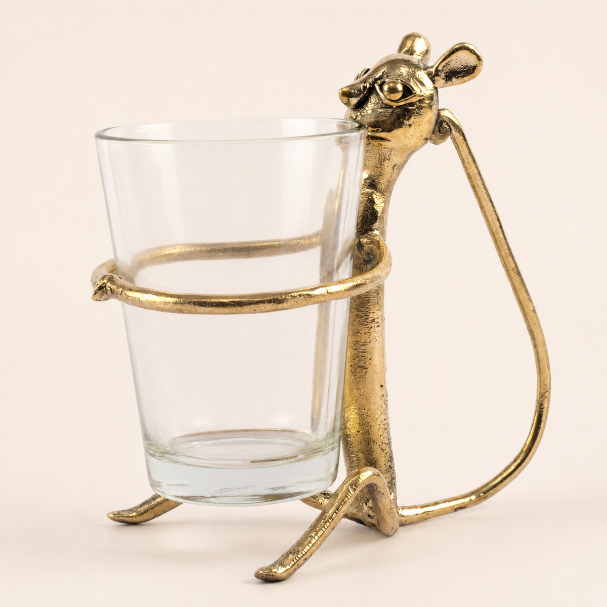 Dhokra brass monkey cup holder with clear glass on a warm ivory studio background