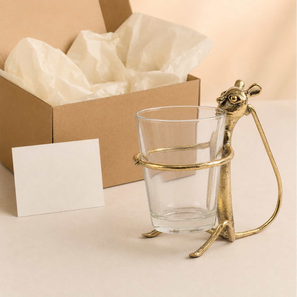 Dhokra brass monkey cup holder with clear glass presented beside a kraft gift box