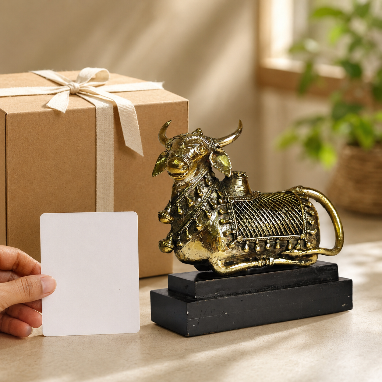 Dhokra Nandi Memento Design 2 beside a kraft gift box with an adult hand holding a blank card for scale