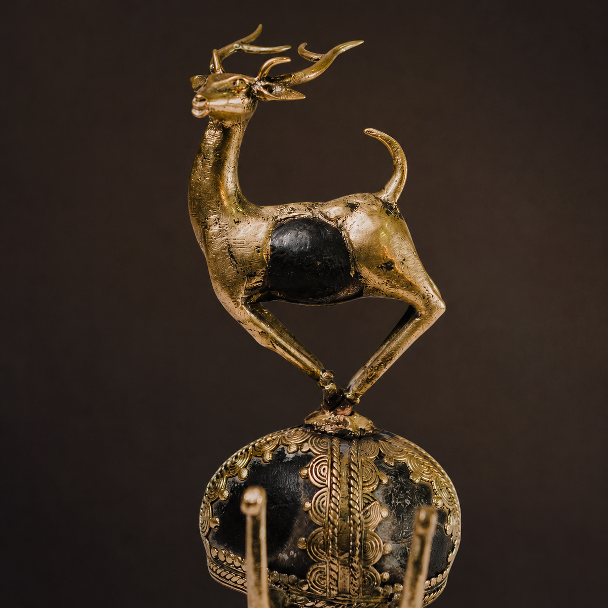 Close detail of the brass patina, embedded black stone and ornate base of a Dhokra deer sculpture