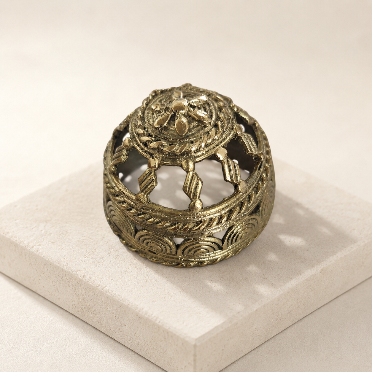 Dhokra Round Paperweight displayed on a warm sandstone plinth