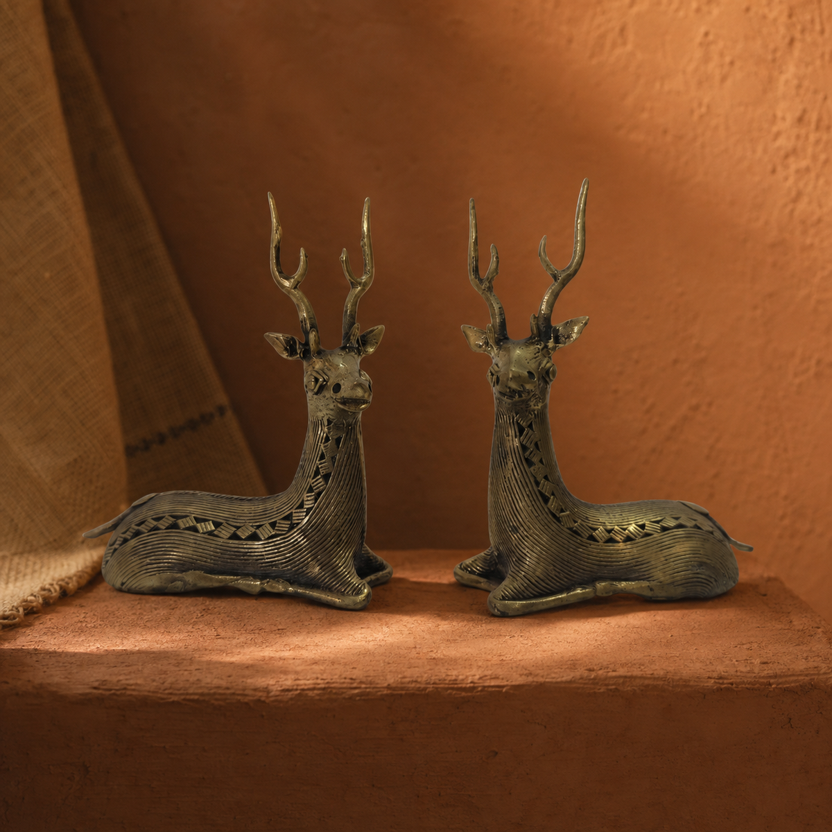 Two-piece Dhokra swamp deer sculpture set on a terracotta plinth in a Bastar-inspired editorial setting