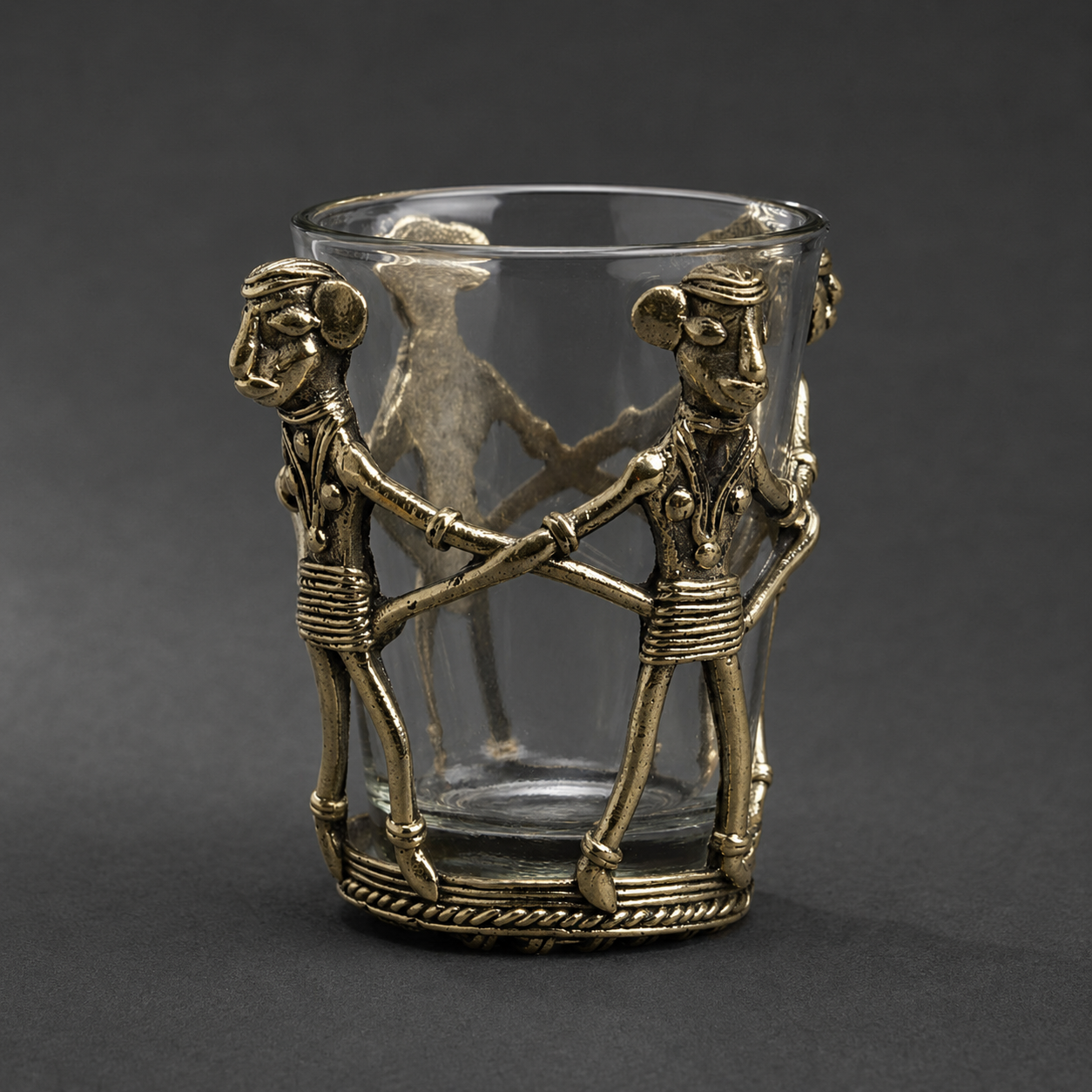 Close product view of the Dhokra tea holder showing linked figures, glass and braided brass base
