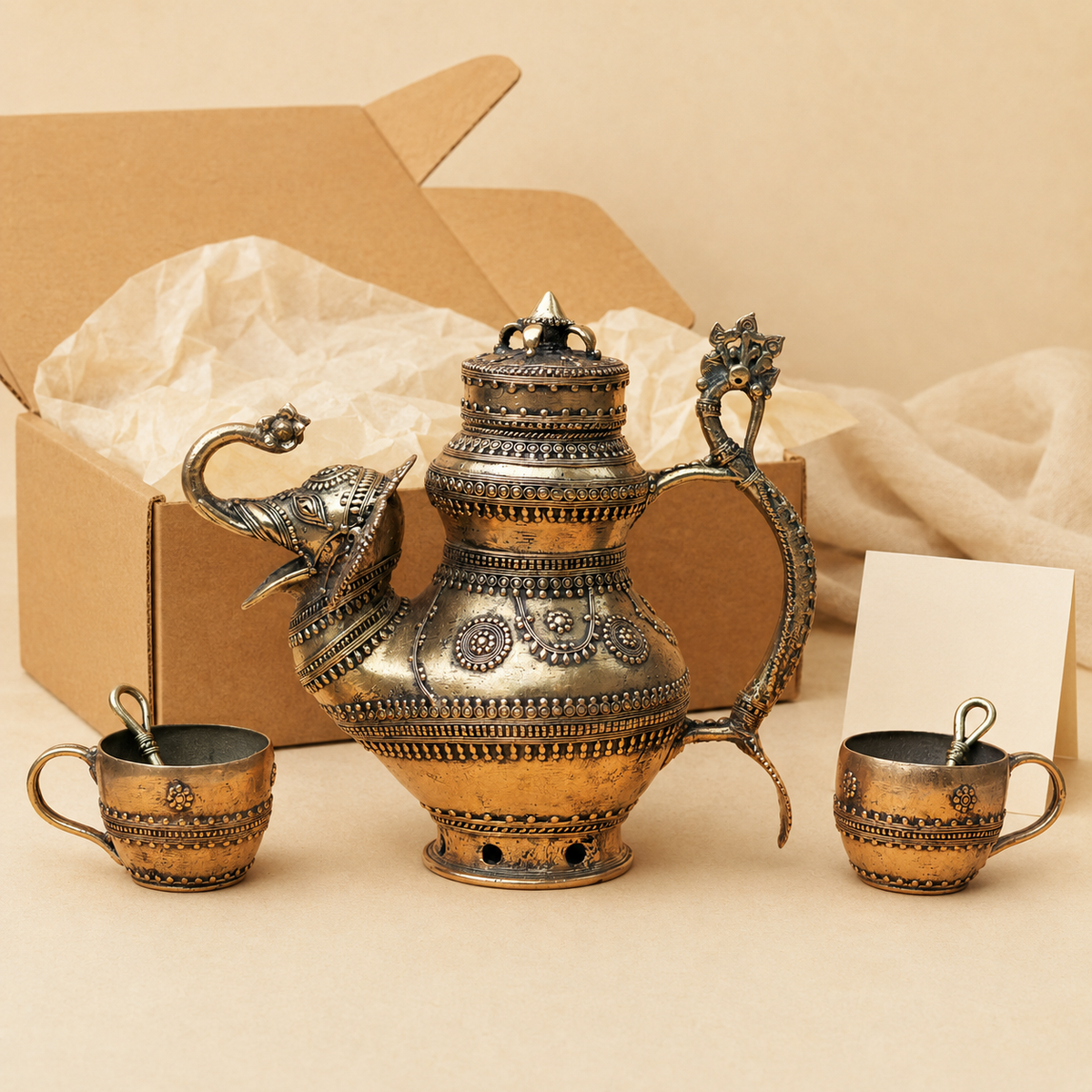 Five-piece Dhokra brass tea set with elephant-spout pot, two cups and two spoons presented beside a gift box