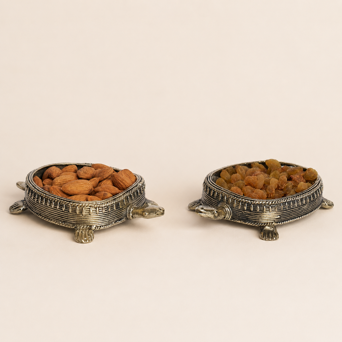 Pair of Dhokra tortoise dry fruit holders with almonds and raisins on an ivory studio background