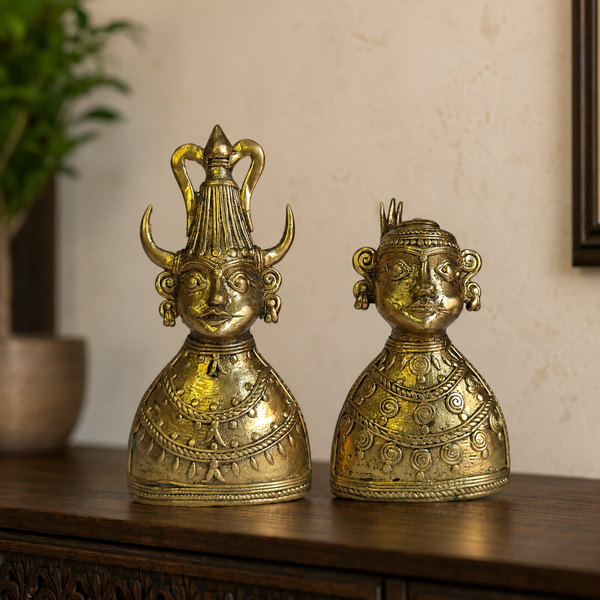 Two Dhokra brass tribal bust figurines displayed together on a dark wood console