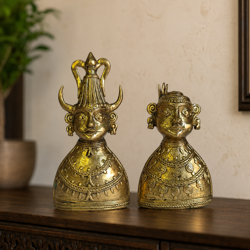 Two Dhokra brass tribal bust figurines displayed together on a dark wood console