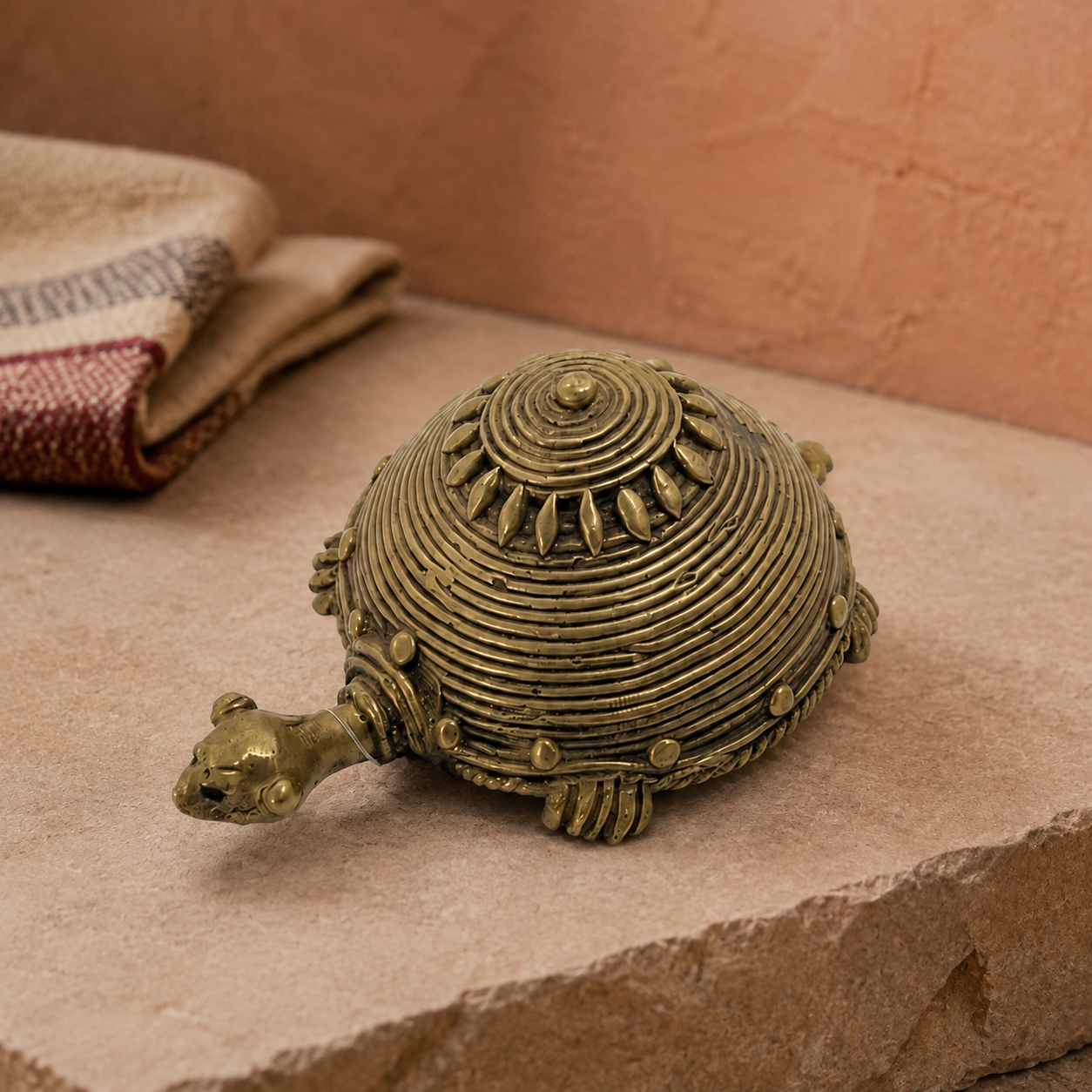 Bastar Dhokra turtle displayed on a stone plinth against a terracotta craft-inspired backdrop