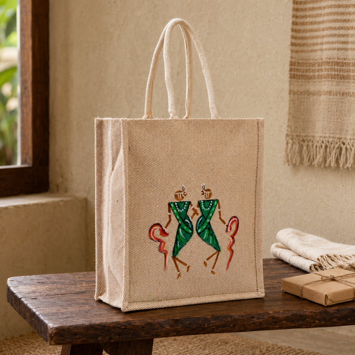 Hand-painted jute tote bag displayed on a wooden bench in a warm natural interior