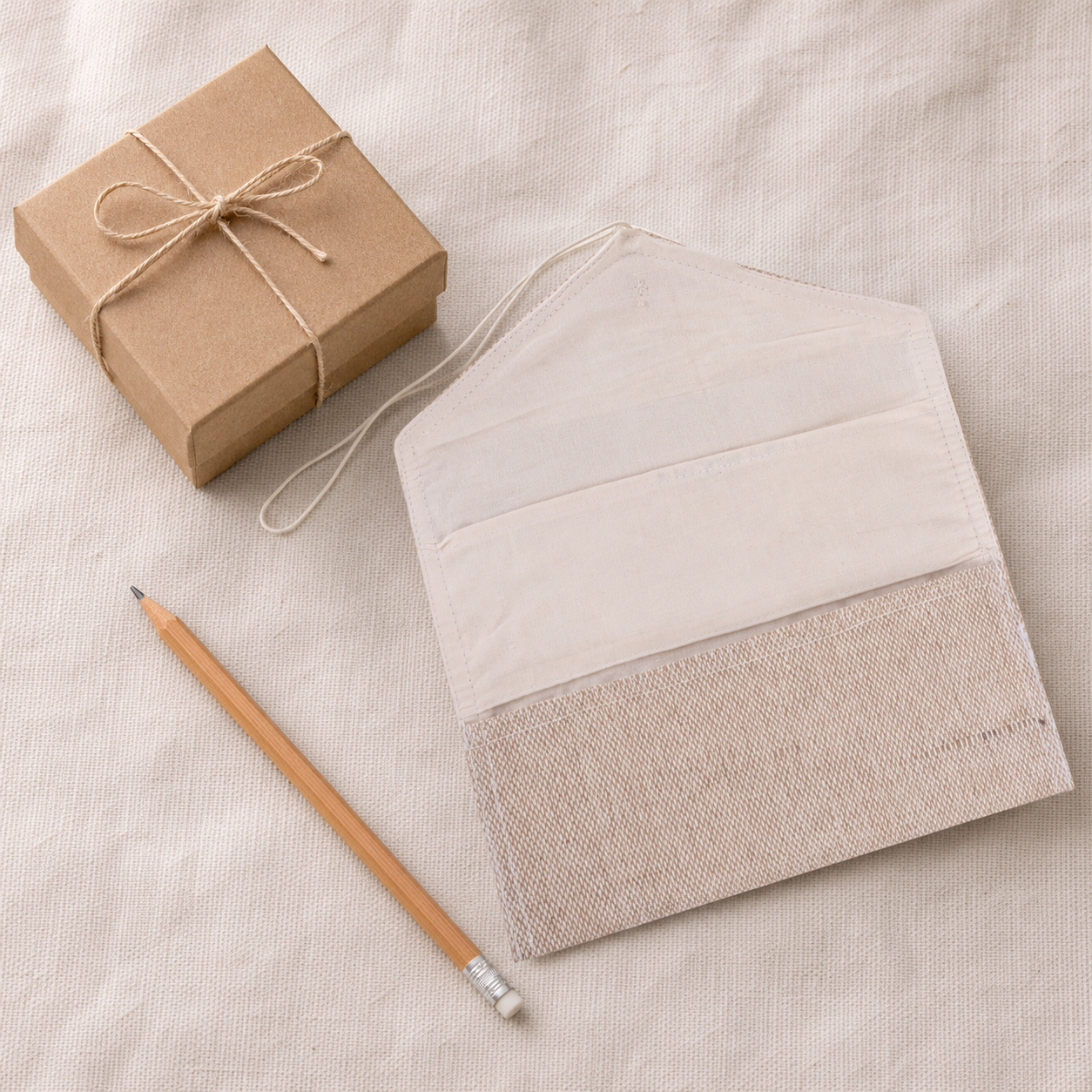 Handcrafted jute fabric pouch beside a kraft gift box and pencil for scale