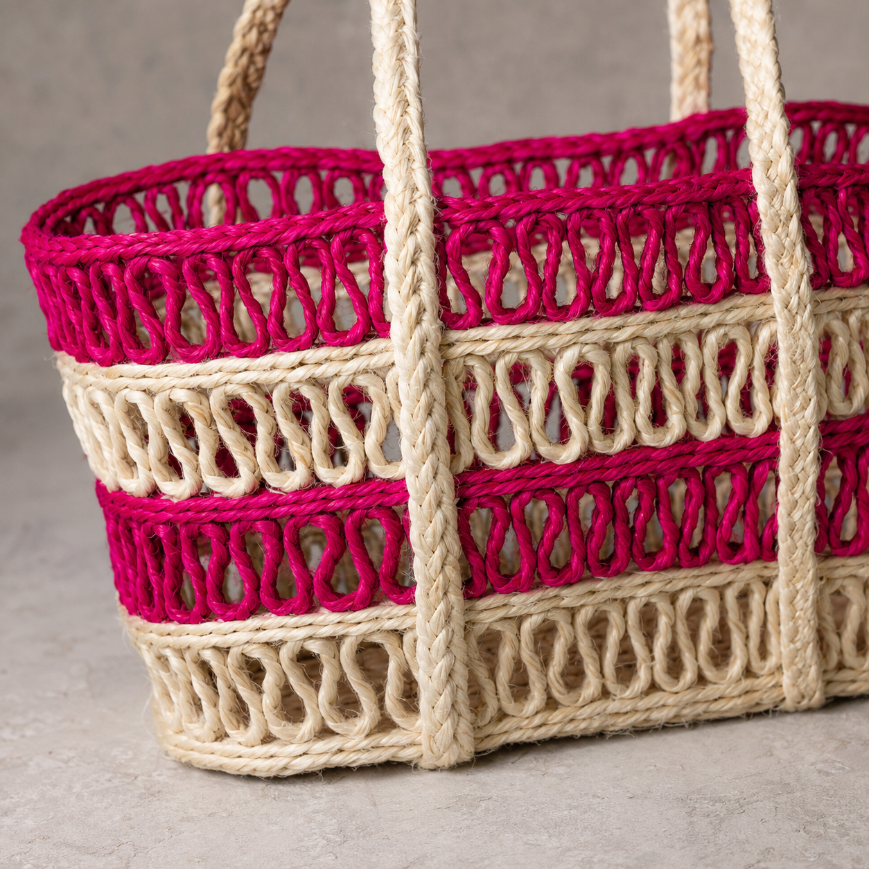 Close detail of the magenta and cream open-loop weave and braided handles of a sisal tote