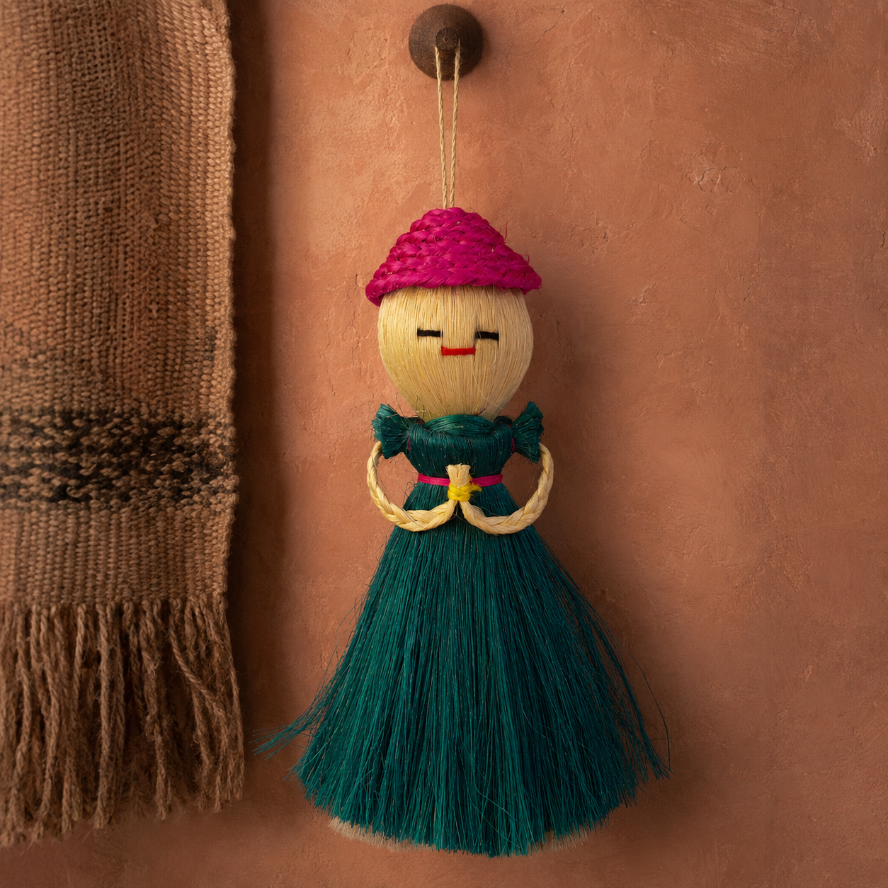 Bastar sisal doll displayed against terracotta plaster with a handwoven textile