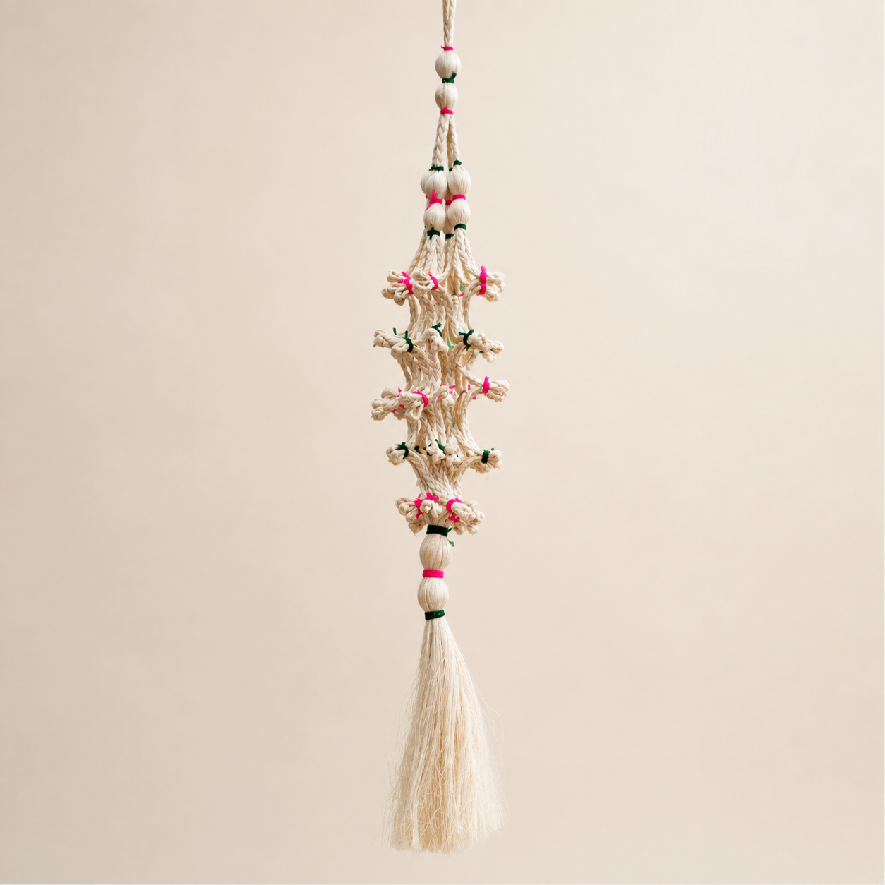 Cream sisal hanging decorative with pink and green bindings on a warm studio background