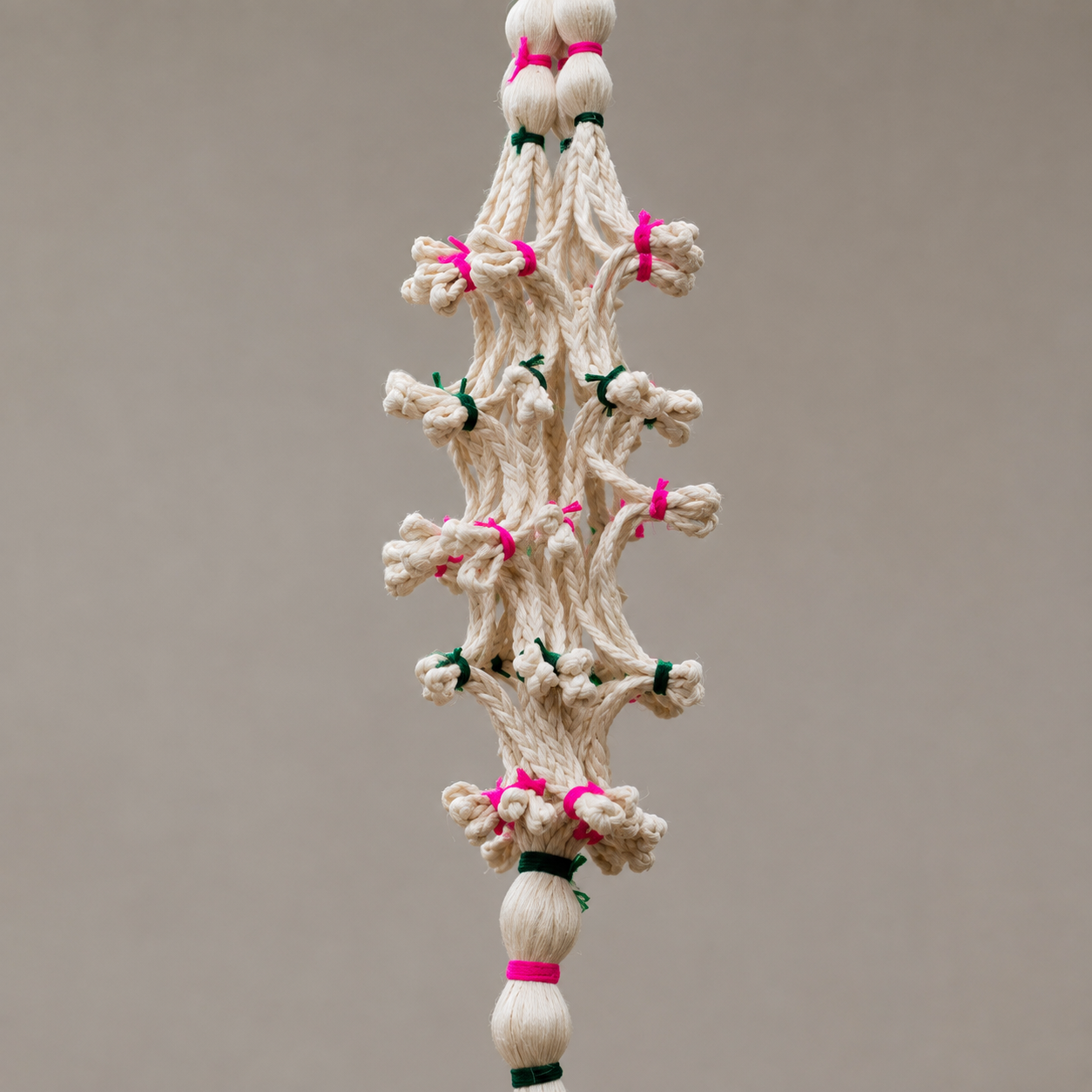 Close detail of hand-knotted cream sisal fibres with pink and green thread bindings