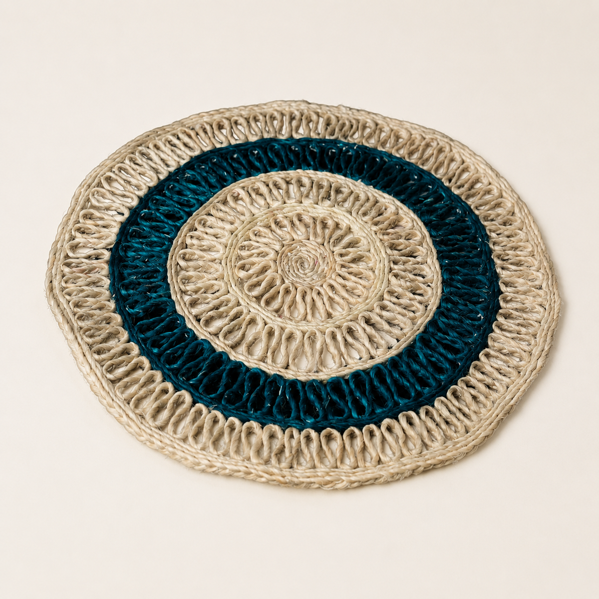 Circular beige and teal sisal table mat on a warm ivory catalogue background