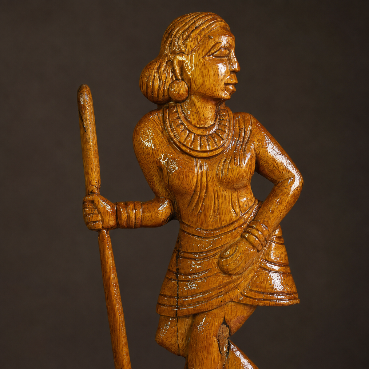Close craftsmanship view of the carved face, jewellery, staff and garment on a wooden Madin sculpture