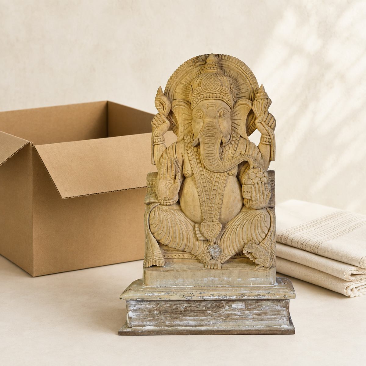 Hand-carved wooden Ganesh statue presented beside a kraft gift box and folded cloth