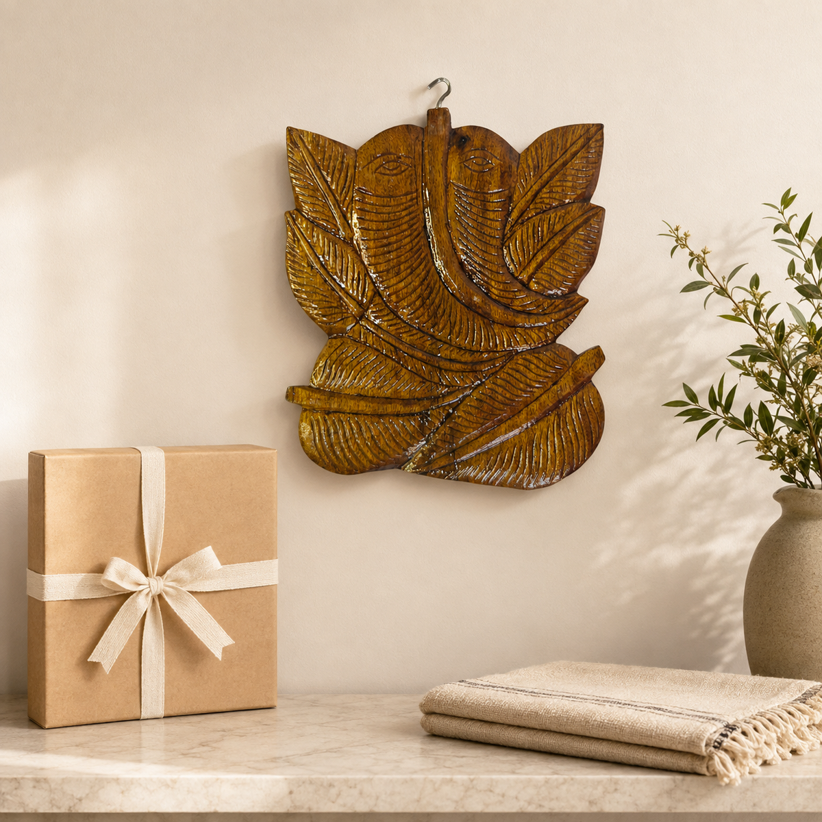 Bastar wooden Ganesha wall hanging presented beside a kraft gift box and handloom cloth