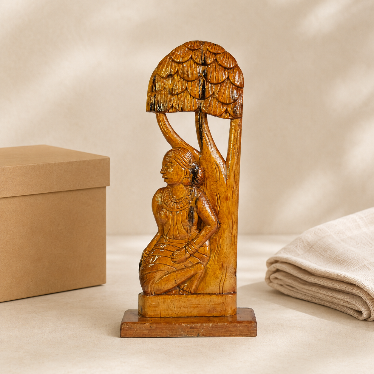 Bastar wood carving of a Madin tribal woman presented beside a kraft gift box and folded cotton cloth