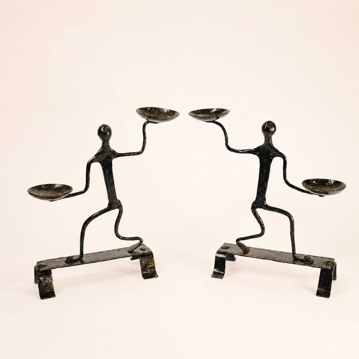 Two-piece Bastar wrought iron dancing figure candle holder with four bowls on an ivory background
