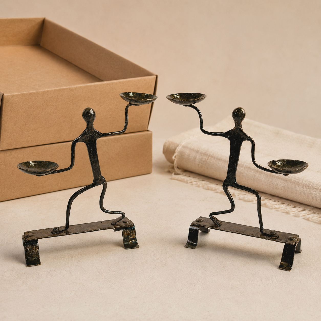 Two Bastar wrought iron dancing-figure candle holders presented beside kraft gift boxes