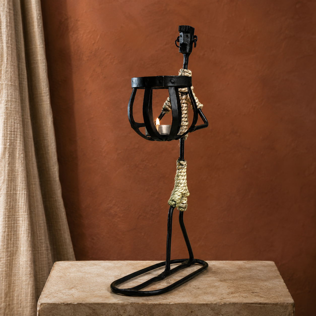Bastar wrought iron tribal candle holder presented on a stone pedestal against a terracotta wall