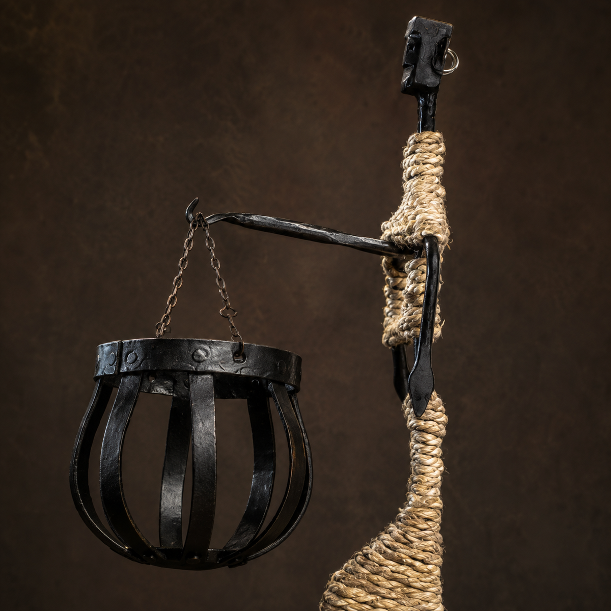 Close detail of the forged arm, suspension chains, riveted basket, and natural rope wrapping