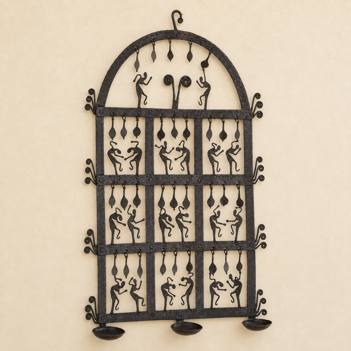 Bastar wrought iron arched diya wall frame with dancing figures and three bowls on an ivory wall