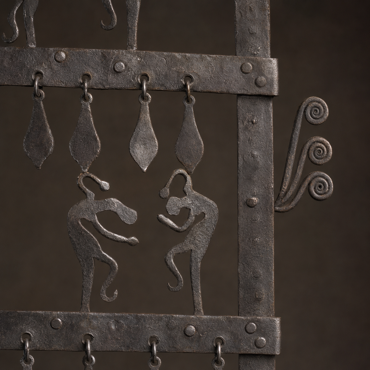 Close detail of riveted rails, dancing figures, leaf pendants, and curled iron scrollwork