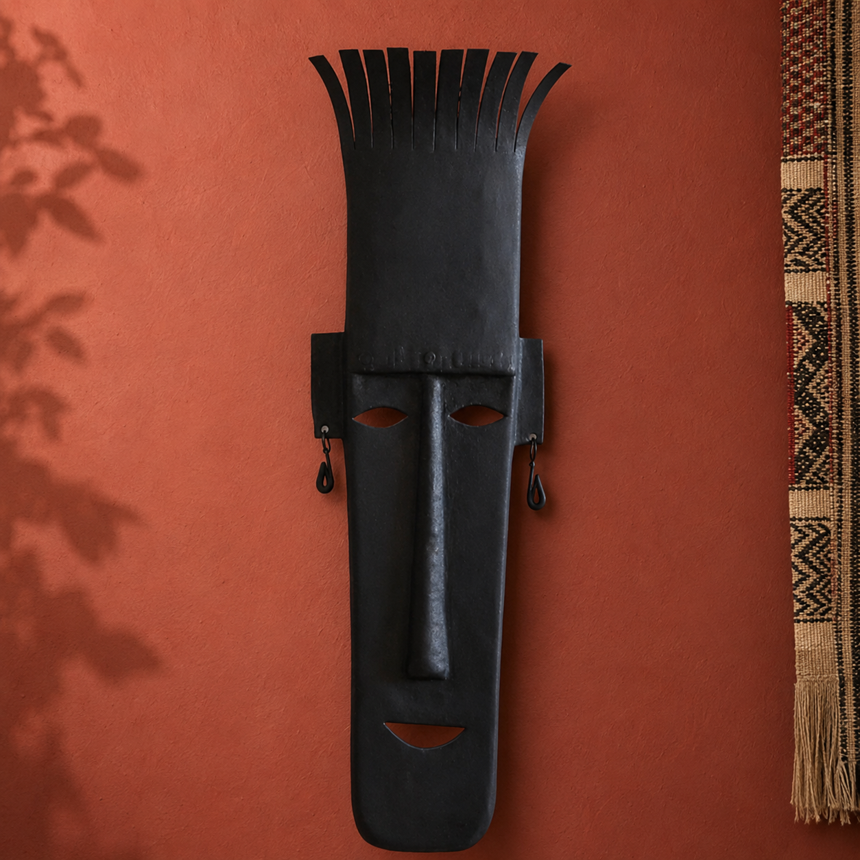Hand-forged Bastar face mask displayed on an ochre gallery wall