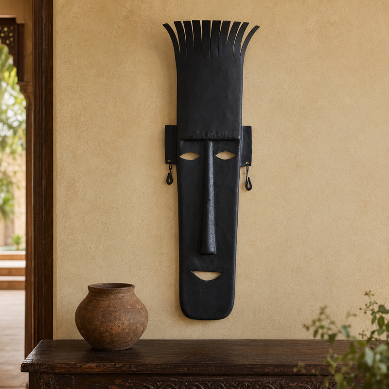 Tall Bastar wrought iron face mask displayed in a warm Indian interior