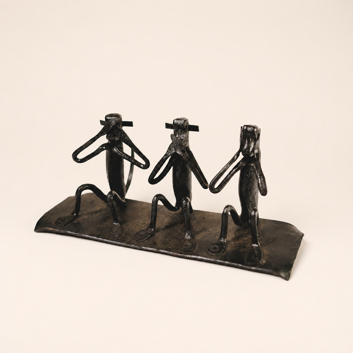 Three wise monkey wrought iron sculpture on a warm ivory catalogue background