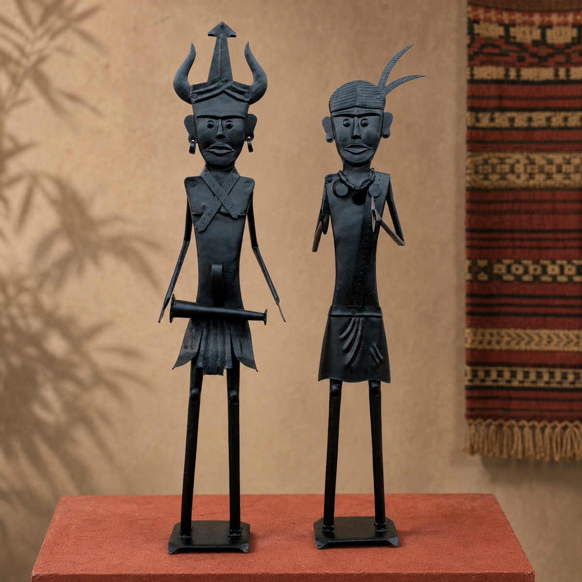 Two handcrafted Bastar iron tribal figures displayed on an ochre gallery plinth